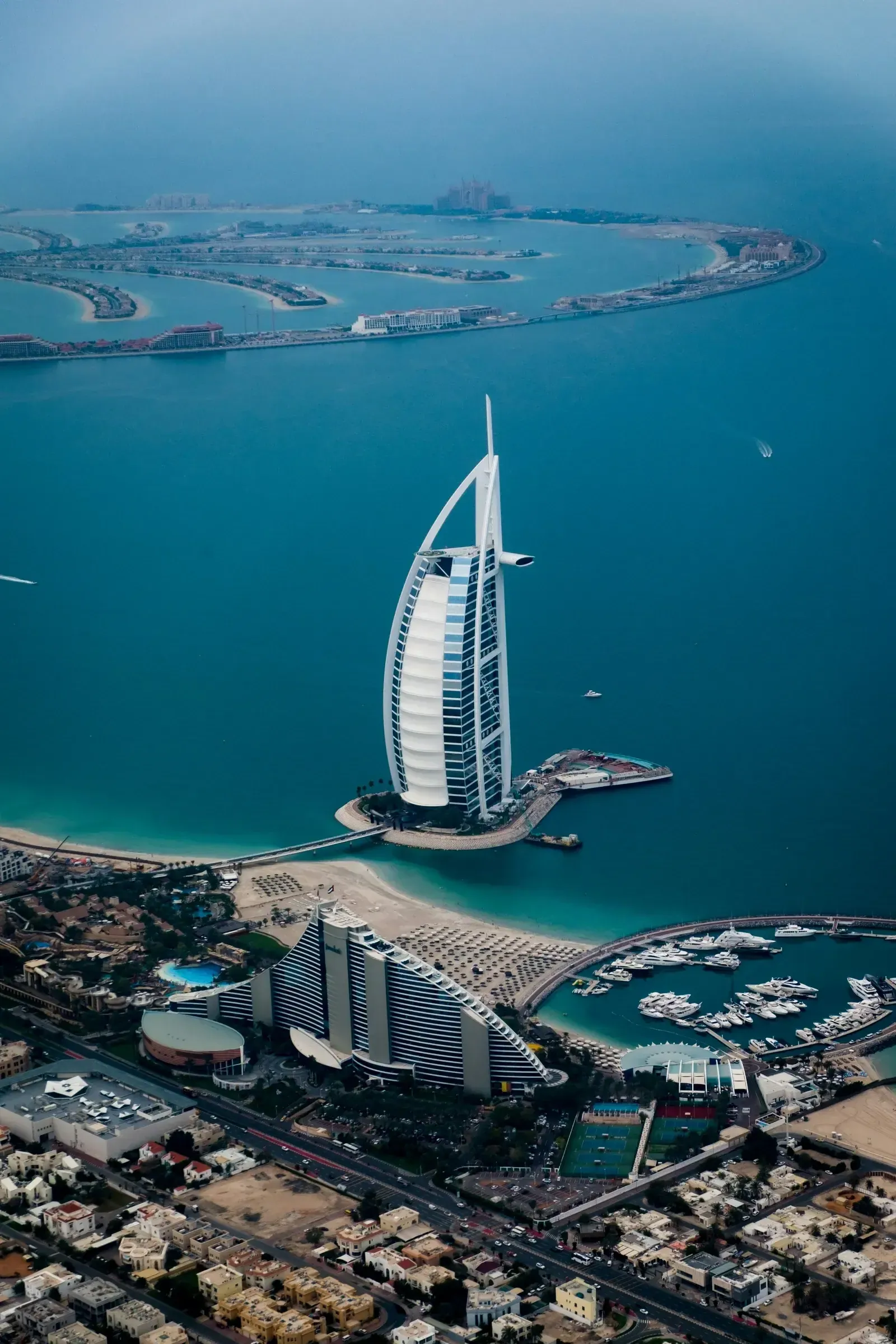Widok z lotu ptaka na Burj Al Arab i wybrzeże Dubaju z Palm Jumeirah w tle — plaża, marina i zabudowa nadmorska